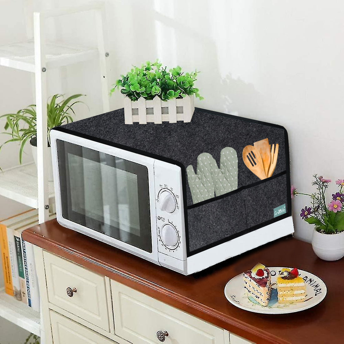 Microwave oven with a black cover on a wooden surface, surrounded by decorative items.