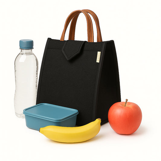 Black tote bag with brown handles, water bottle, blue container, banana, and apple on a white background