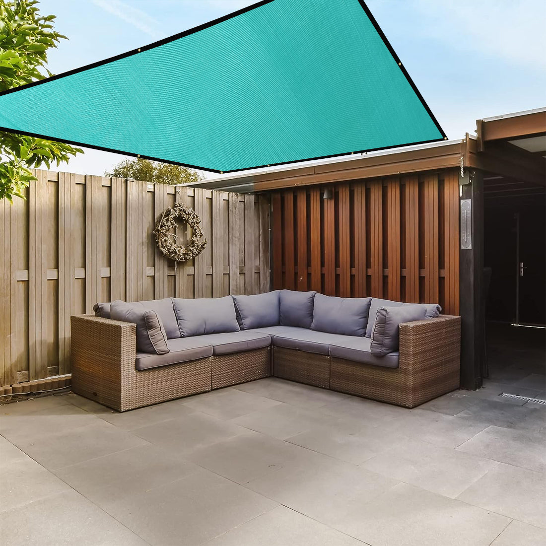 Outdoor patio with wicker sectional sofa, teal shade sail, and wooden fence.