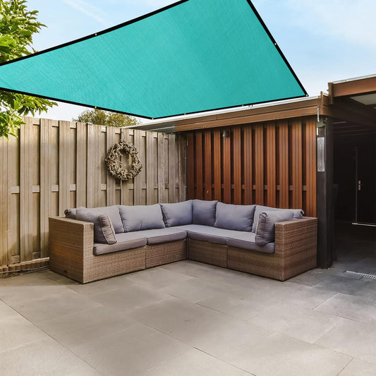 Outdoor patio with wicker sectional sofa, teal shade sail, and wooden fence.