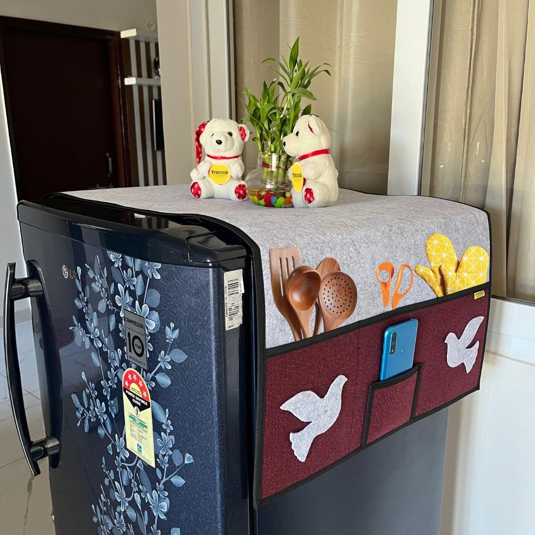 Fridge with a decorative cover featuring pockets, utensils, and toys.