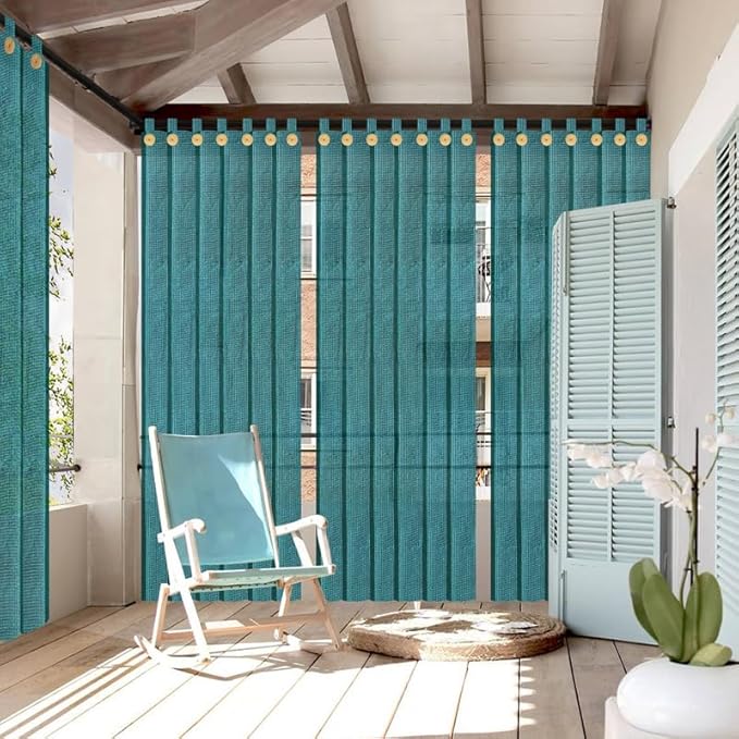 Teal outdoor curtains with decorative rings in a patio setting with a rocking chair and plant.